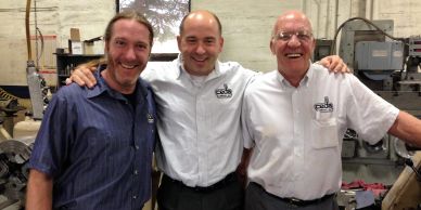 Three men smiling together in a workshop.