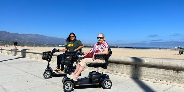 Two mobility scooter rental users on sidewalk near west beach