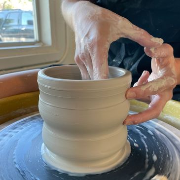 Hands throwing a large piece of pottery on the wheel.