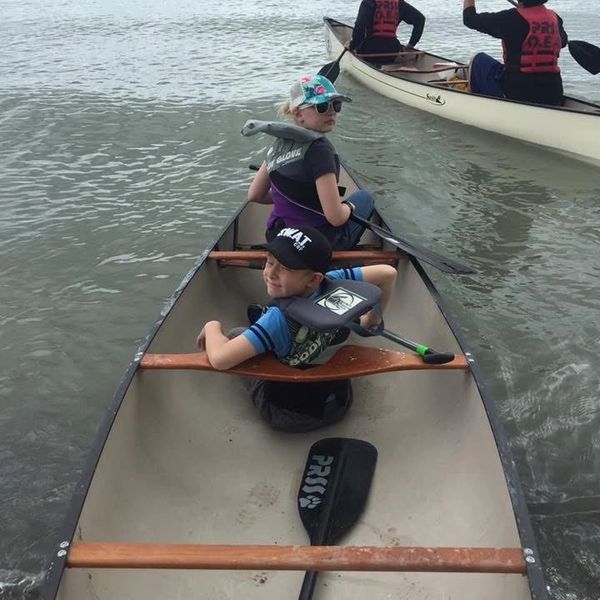 Two children in a canoe preparing to paddle on the water.