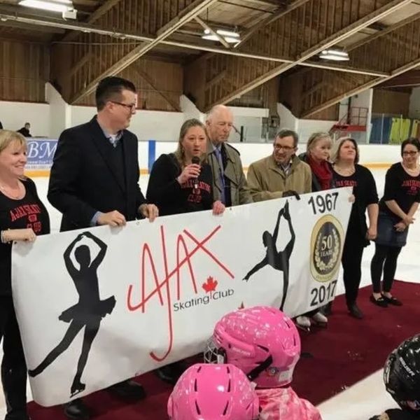 A group holding a banner celebrating Ajax Skating Club's 50th anniversary on an ice rink.