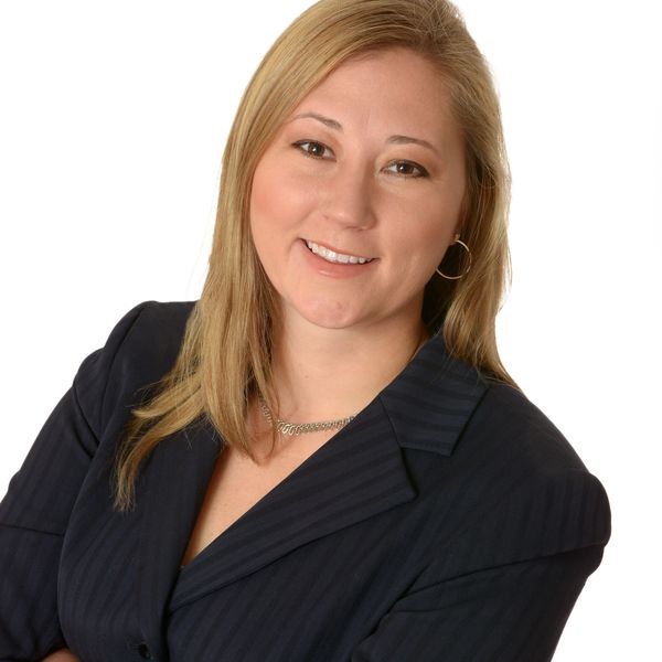 Professional woman smiling confidently in a dark blazer against a white background.