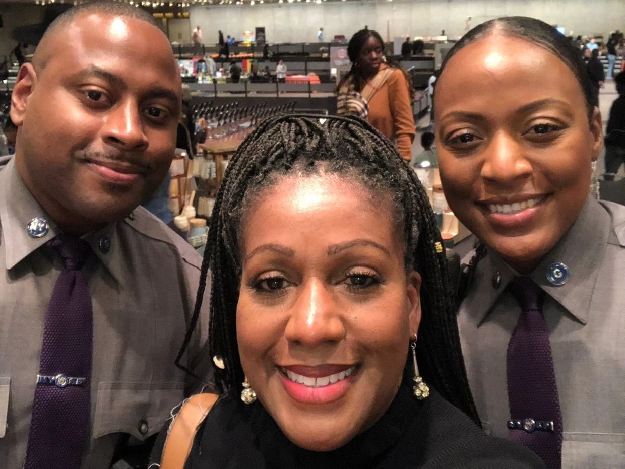 Three people smiling in a close-up selfie, two in uniform.