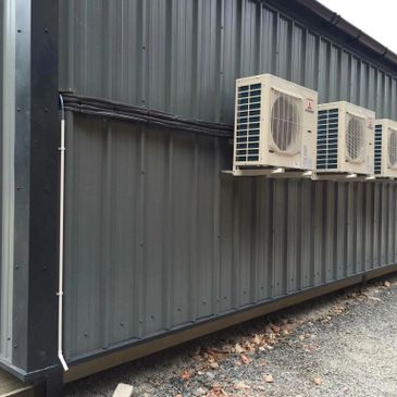 Four air conditioning units mounted on a gray metal building exterior Hereford.