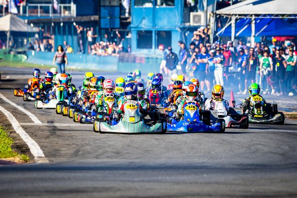 Go-kart racers competing intensely on a track with spectators in the background.