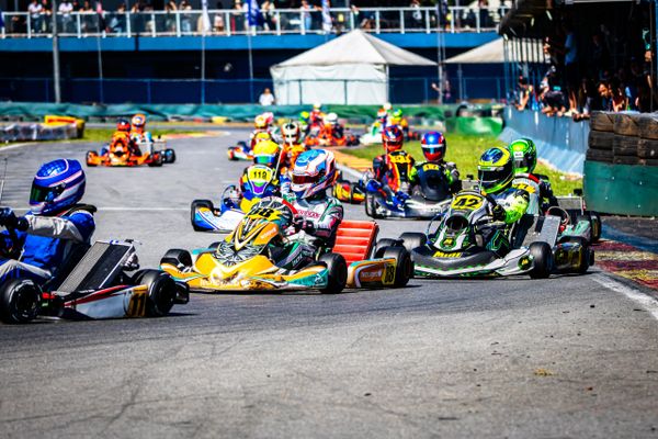 Go-kart racers compete closely on a sunny race track.