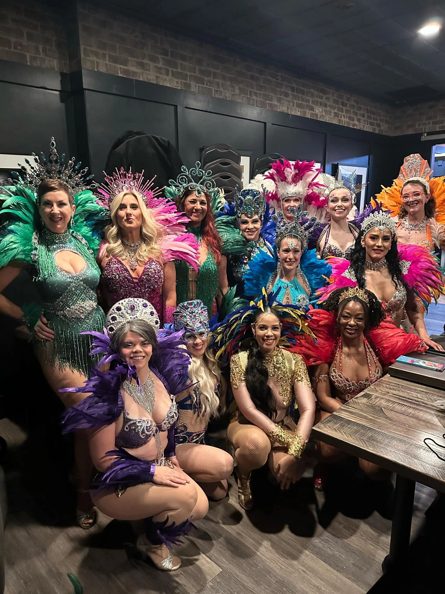 Group of women in colorful feathered costumes and jeweled headpieces.