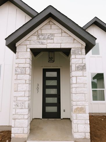 Modern house entrance with stone pillars and black door.