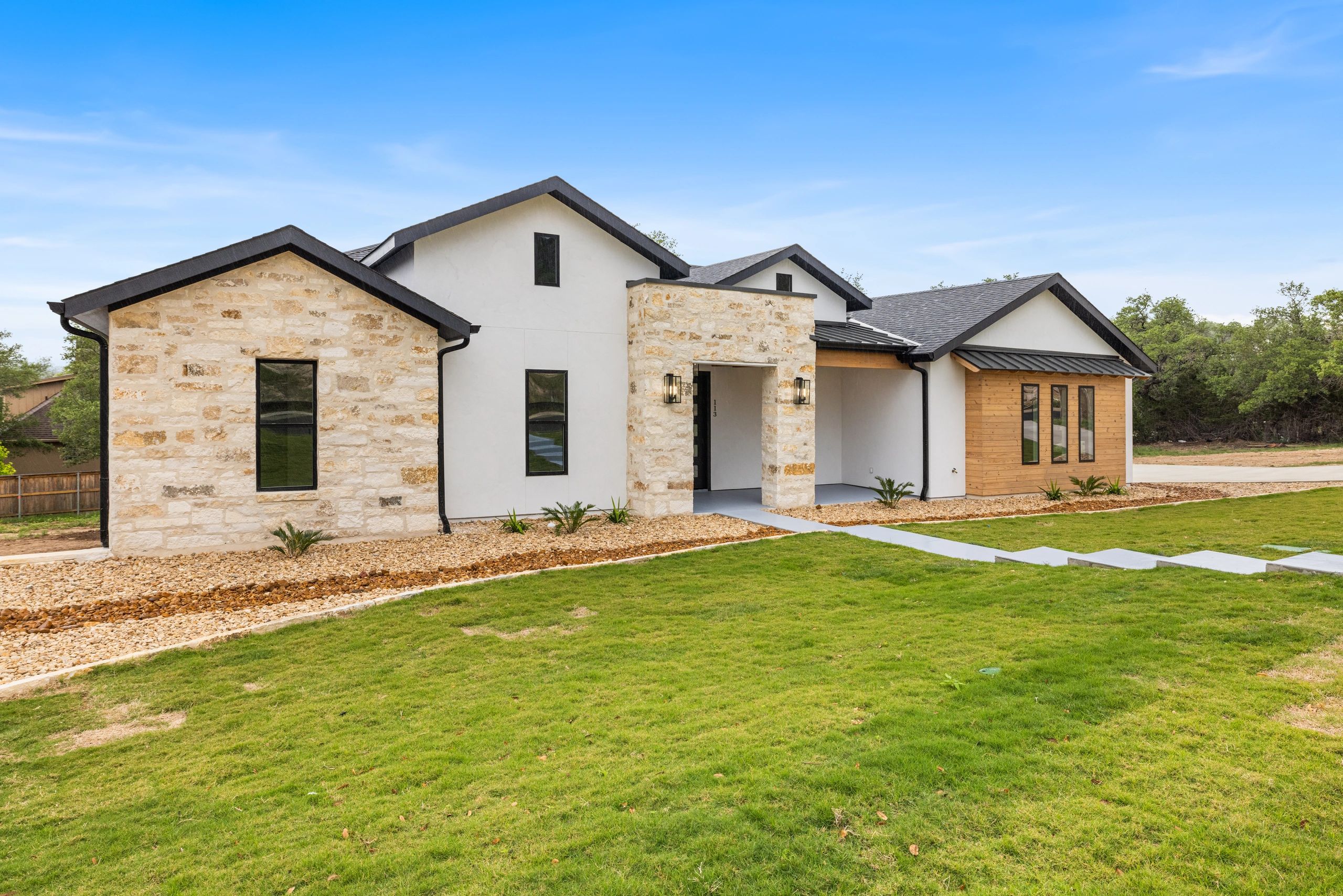 Modern house with stone and wood exterior and a green lawn.