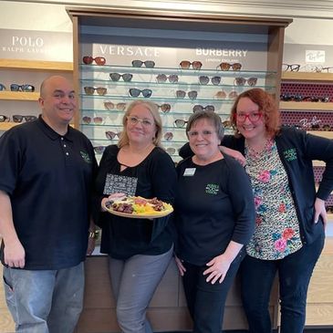 Four people wearing black Pearle Vision uniform shirts stand together in front of a frame board.