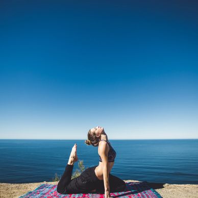 A woman practices yoga by the ocean under a clear blue sky.