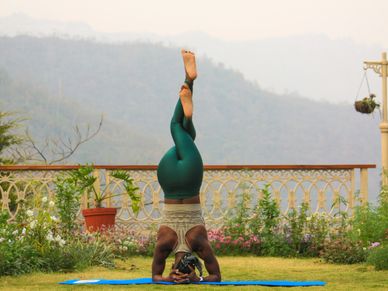 Person practicing a headstand yoga pose outdoors on grass.