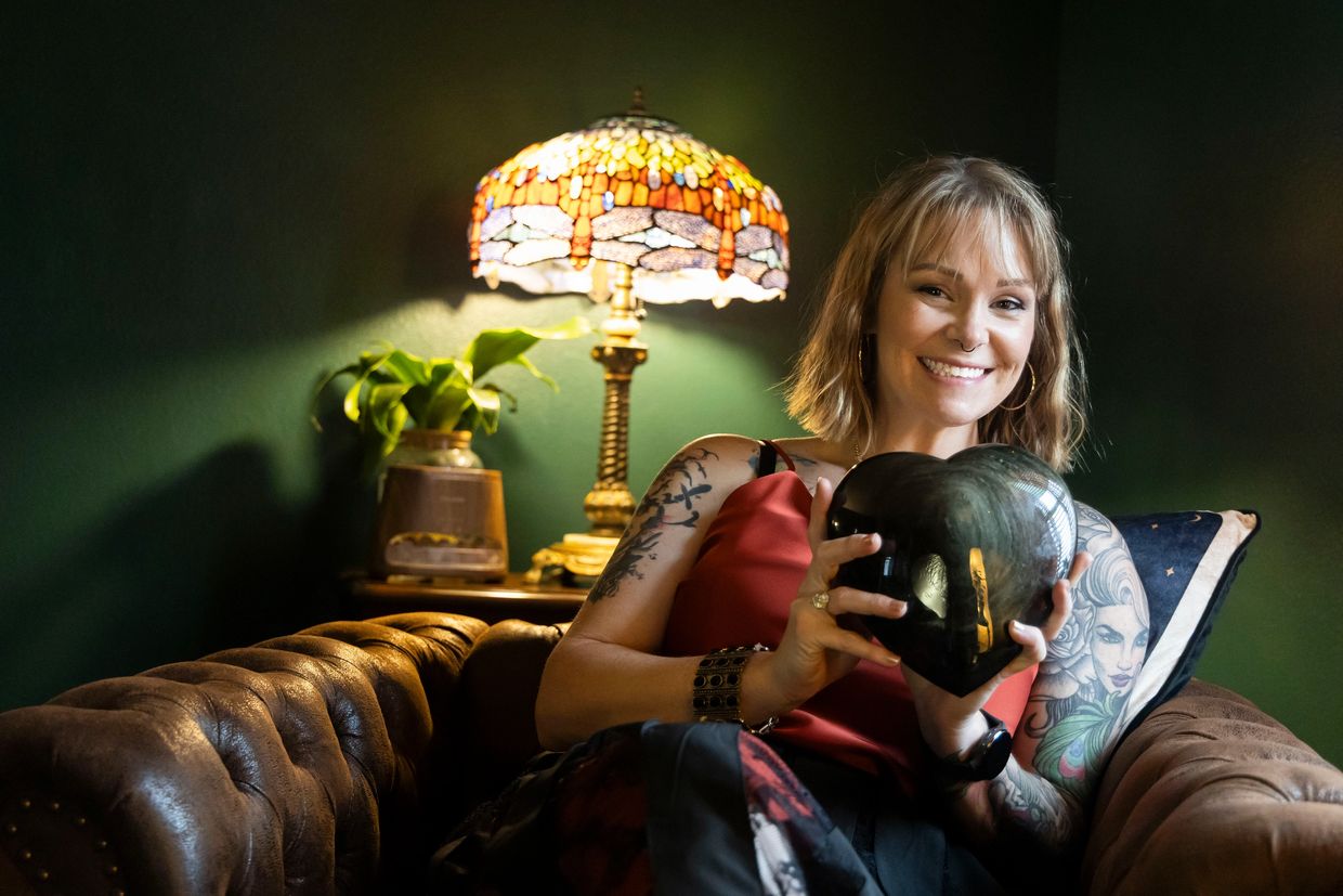 Woman smiling, holding a dark heart-shaped object on a brown leather couch.