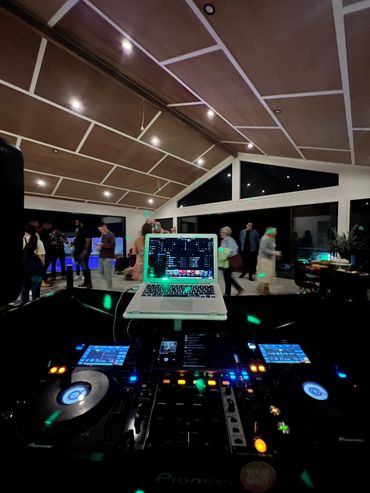 DJ setup with a laptop and turntables at a lively indoor party.