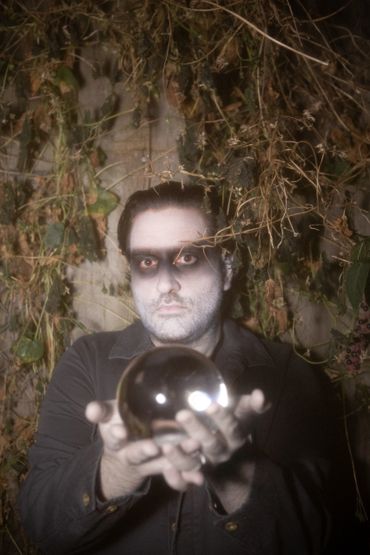 a dream ghoul peers into the camera with its hands outstretched, holding a crystal ball up. 