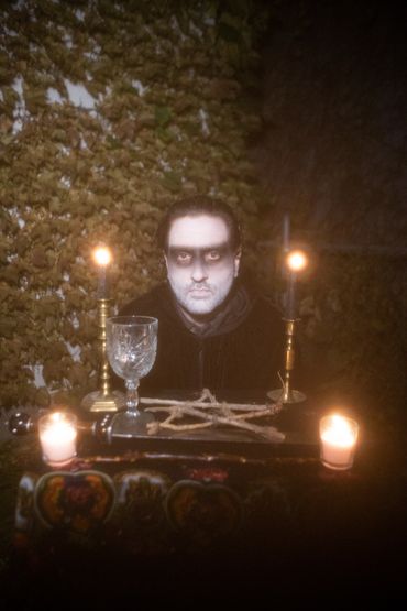 a dream ghoul sits behind an altar with the pentacle, sword, wand, and chalice. it is the magician.