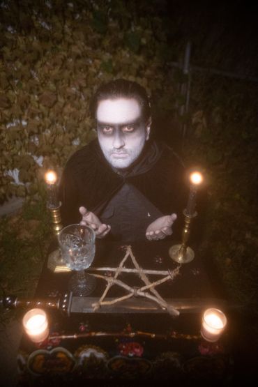 a dream ghoul kneels behind an altar with a pentagram, sword, wand, and chalice. it is the magician. 