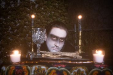 a dream ghoul kneels with its head rested on an altar covered with a pentagram, sword, chalice, wand.