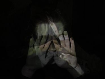 a dream ghoul holds up the palms of its hands over its eyes. an image is projected on the hands.