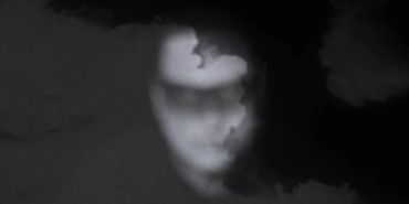 the face of a dream ghoul is obscured and blurred by smoke, blending into a black background. 