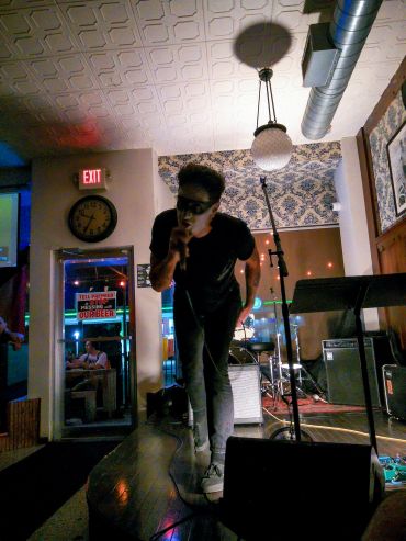 Man singing into a microphone at a small indoor venue.