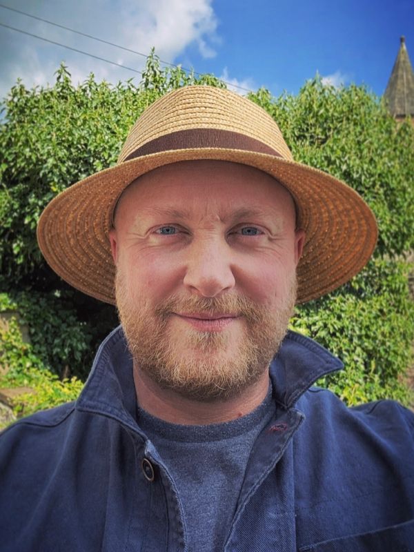 Man wearing a straw hat and blue jacket outdoors on a sunny day.