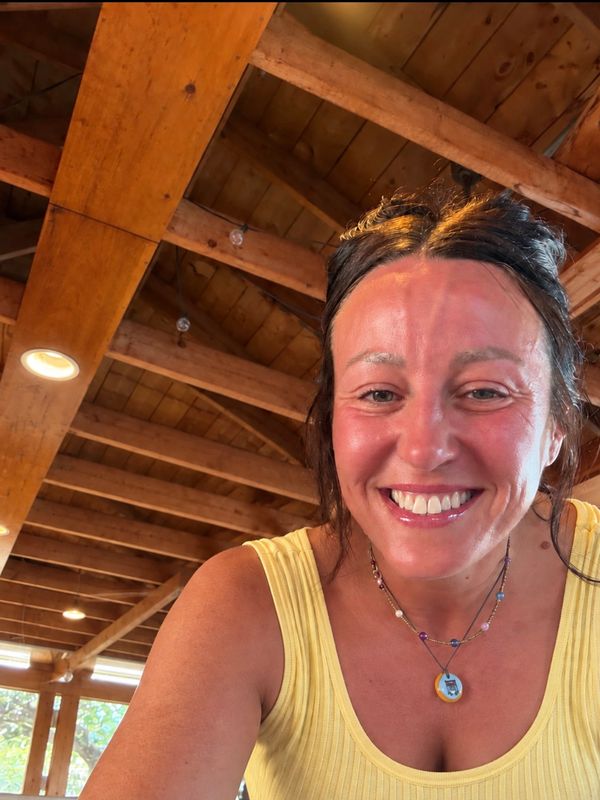 Smiling woman in yellow tank top with wooden ceiling background.