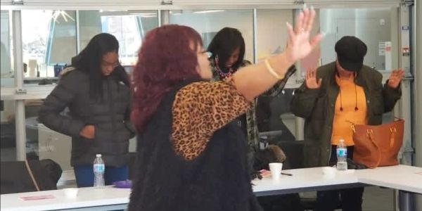 A group of women engaging in a moment of prayer or reflection in a meeting room.