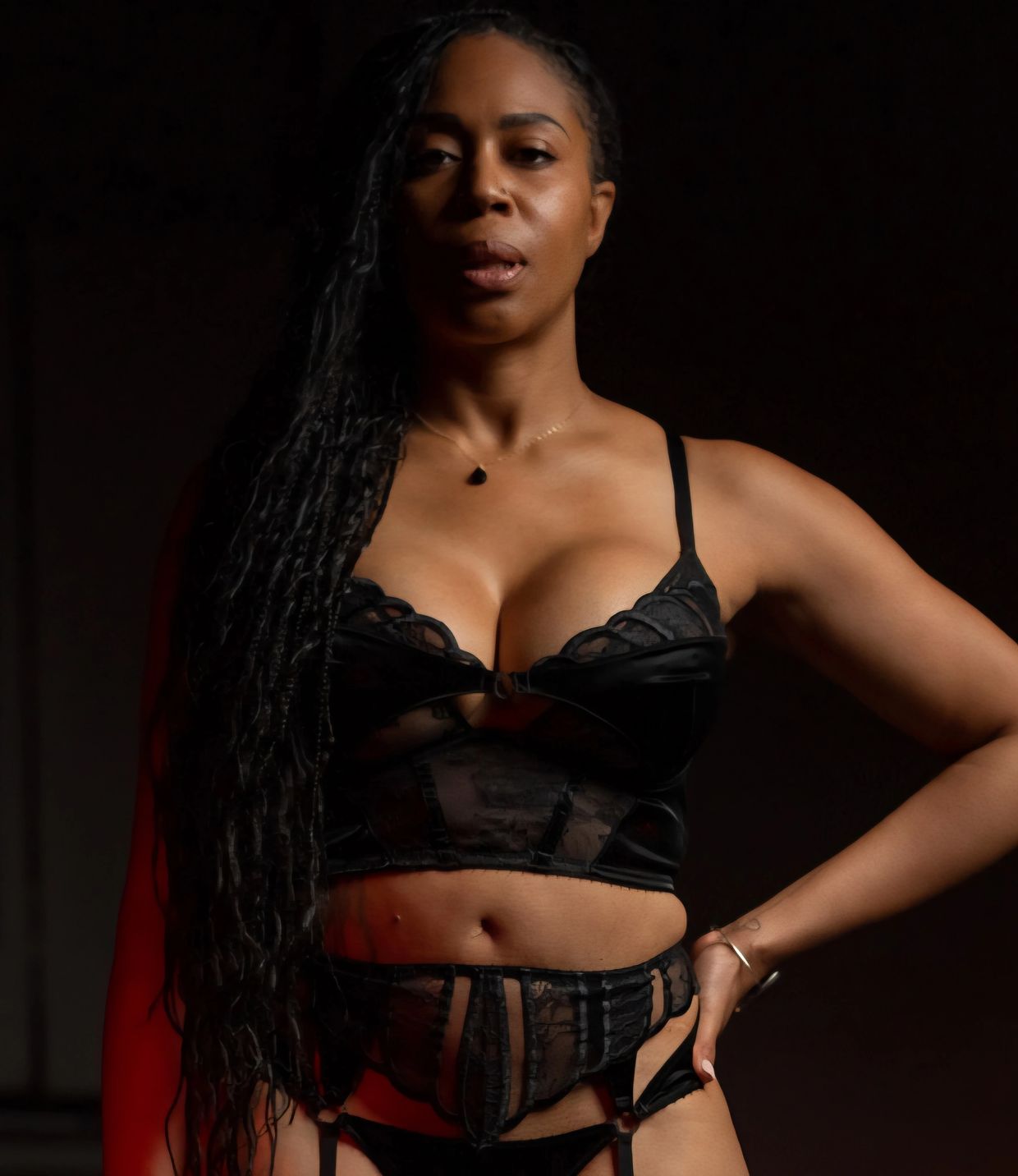 Confident woman posing in black lace lingerie against a dark background.