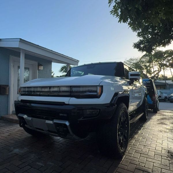 A white GMC Hummer EV parked on a driveway during sunset.