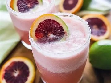 Two pink citrus cocktails garnished with blood orange slices and salt rims.