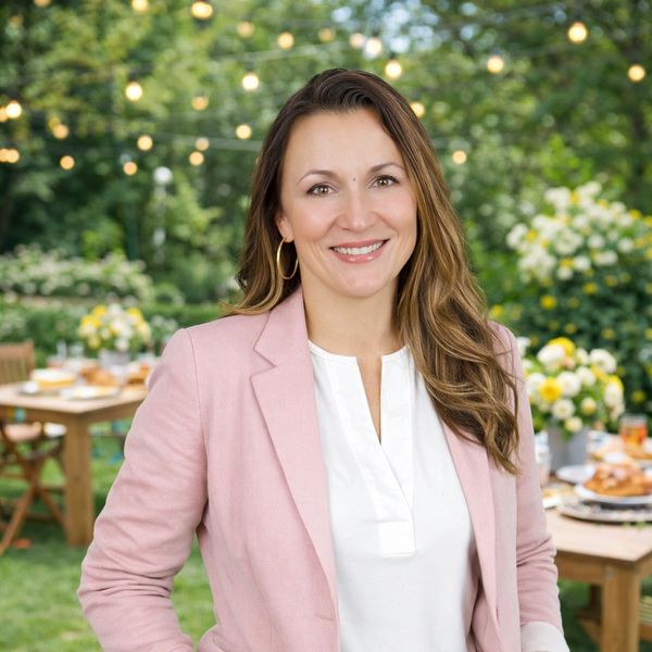 Smiling woman in pink blazer at an outdoor garden gathering.