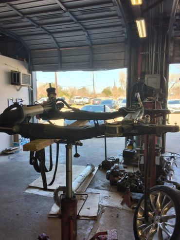 Car steering rack and suspension parts in a garage workshop.