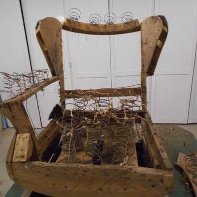 Old wooden chair frame with exposed springs and worn upholstery.