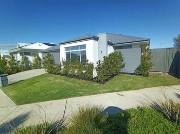 Modern single-story house with a neat lawn and shrubs under a clear blue sky.