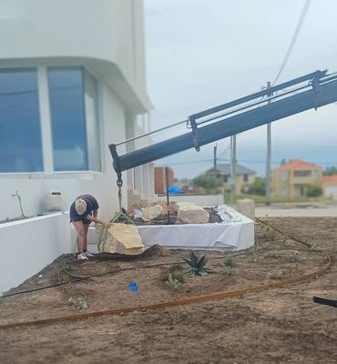 Person positioning large rocks with a crane near a modern house.