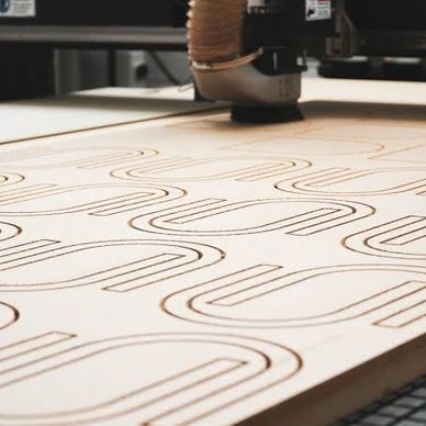 A CNC machine cutting curved patterns into a flat wooden sheet.