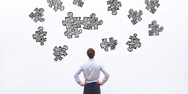 Man staring at white board showing puzzle pieces that are scattered.