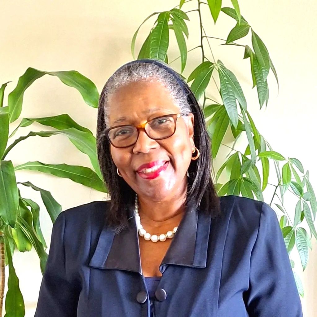 Smiling woman in glasses and pearl necklace with green plants background.