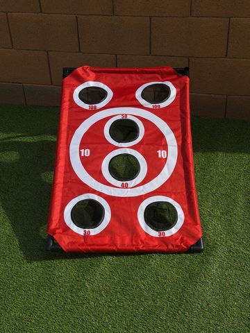 Red bean bag toss game with various scoring holes on green turf.
