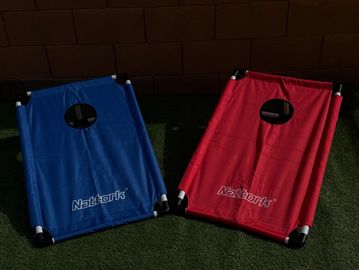 Two cornhole boards, one blue and one red, set up on grass.