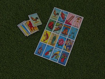 A set of colorful Lotería game cards spread on green grass.