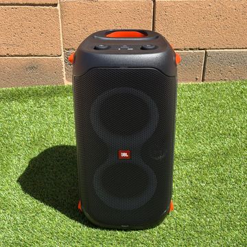 JBL portable speaker on grass with a brick wall background.