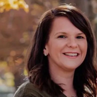 Smiling woman with dark hair outdoors in autumn light.