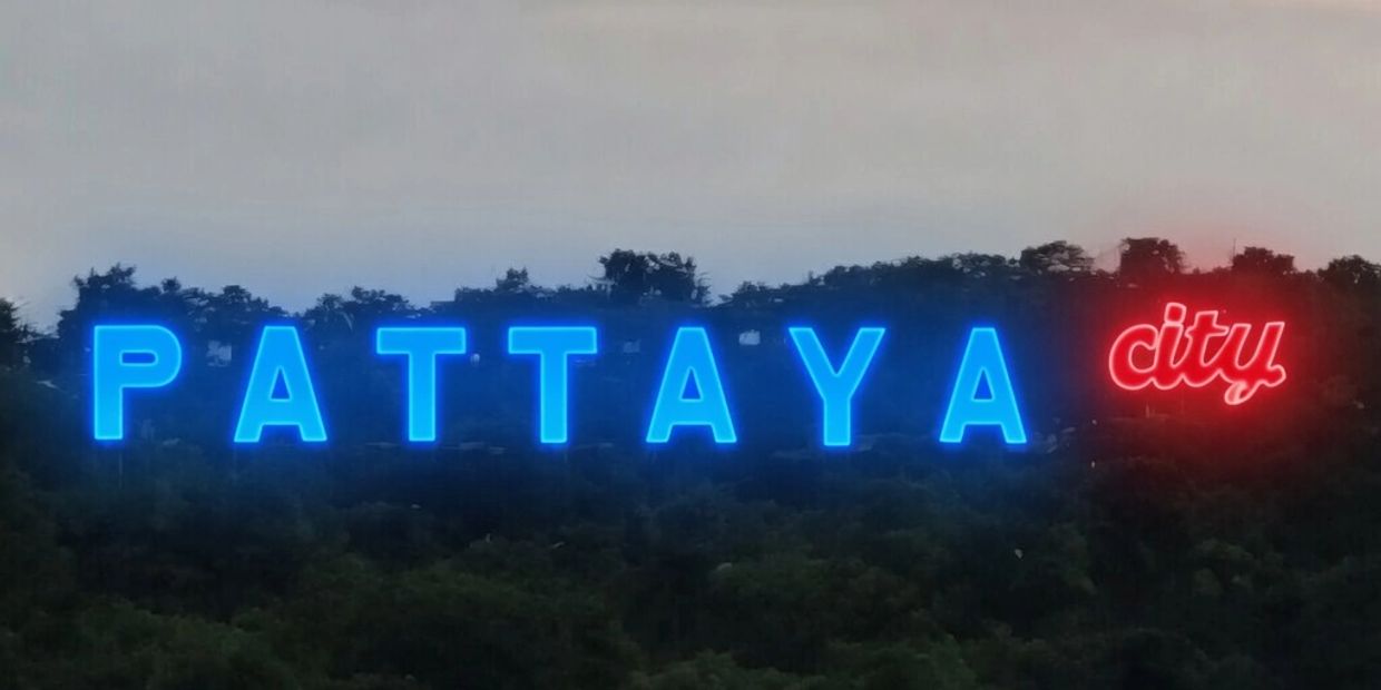 Neon sign displaying "PATTAYA city" on a hillside at dusk.
