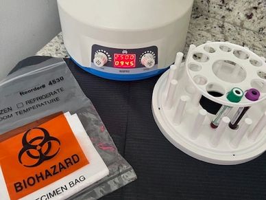Laboratory centrifuge with specimen tubes and a biohazard specimen bag on a countertop.