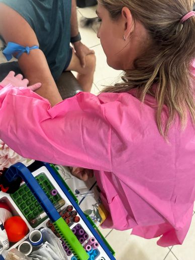 Healthcare worker in pink coat preparing to draw blood from patient with blue tourniquet.