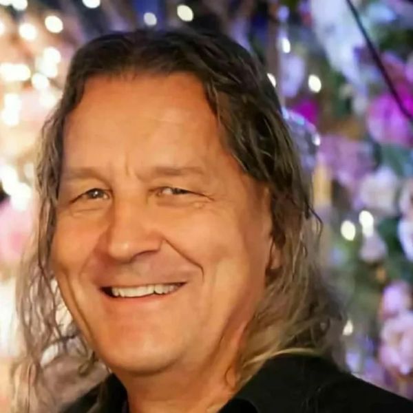 Smiling man with long hair in a softly lit setting.