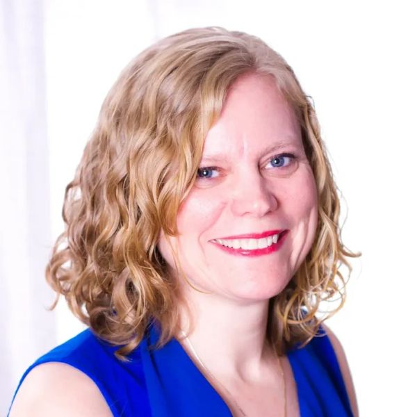 Smiling woman with curly blonde hair in a blue outfit.