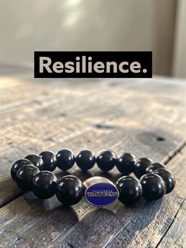 Black beaded bracelet with Baltimore Ravens emblem on wooden surface.